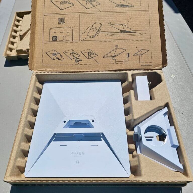 Starlink Mini unboxed with pole mount and accessories in cardboard packaging.
