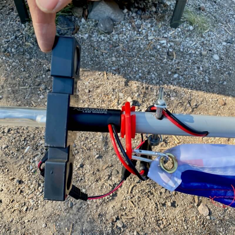 Close-up showing how to attach a flag and a camp locator light to an RV flagpole with correct ring placement and wiring.