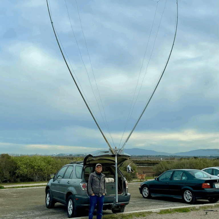 Hiroki Kato, AH6CY, stands in front of his fully deployed portable 4-band delta loop antenna mounted on the hitch of his vehicle.