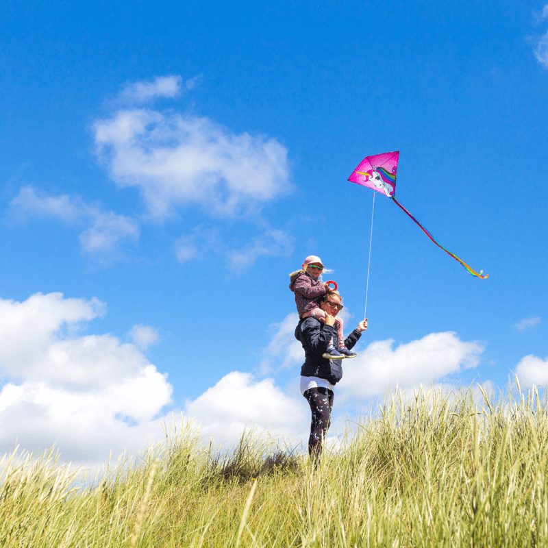 A mother with her child on her shoulders, flying a kite together and creating a lasting memory.