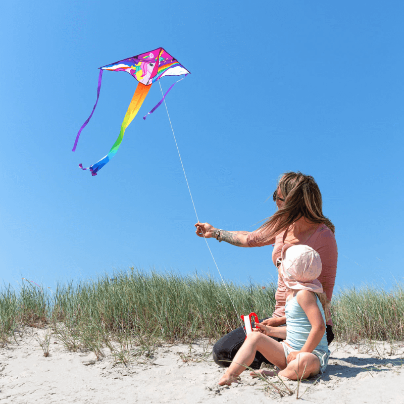 A mother and child on a sandy dune, flying a colorful kite, enjoying screen-free camping activities for kids.