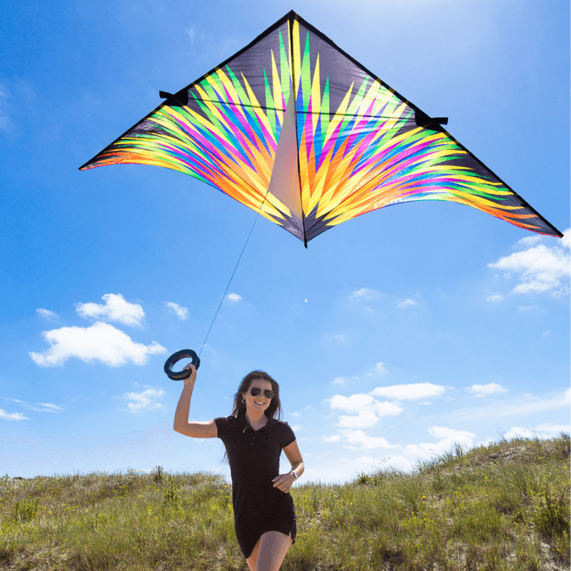 A smiling woman runs through a grassy field while flying a large, vibrant kite, demonstrating the fun of kite flying at campgrounds.