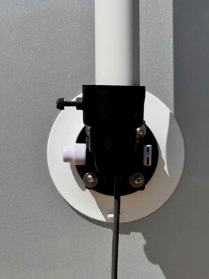 A straight-on close-up of the RV Flag Pole Buddy Suction Cup Mount 2.0 showing the vacuum plunger, pole thumbscrew, and a black cable running from the pole.