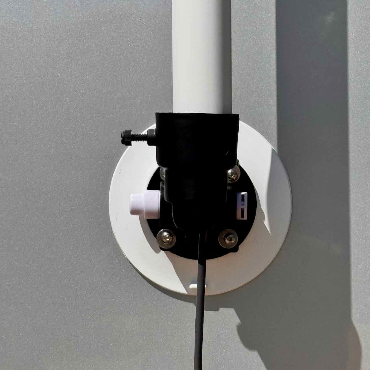 A straight-on close-up of the RV Flag Pole Buddy Suction Cup Mount 2.0 showing the vacuum plunger, pole thumbscrew, and a black cable running from the pole.